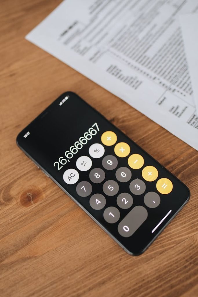 Close-up of smartphone calculator app and tax forms on a wooden desk surface.