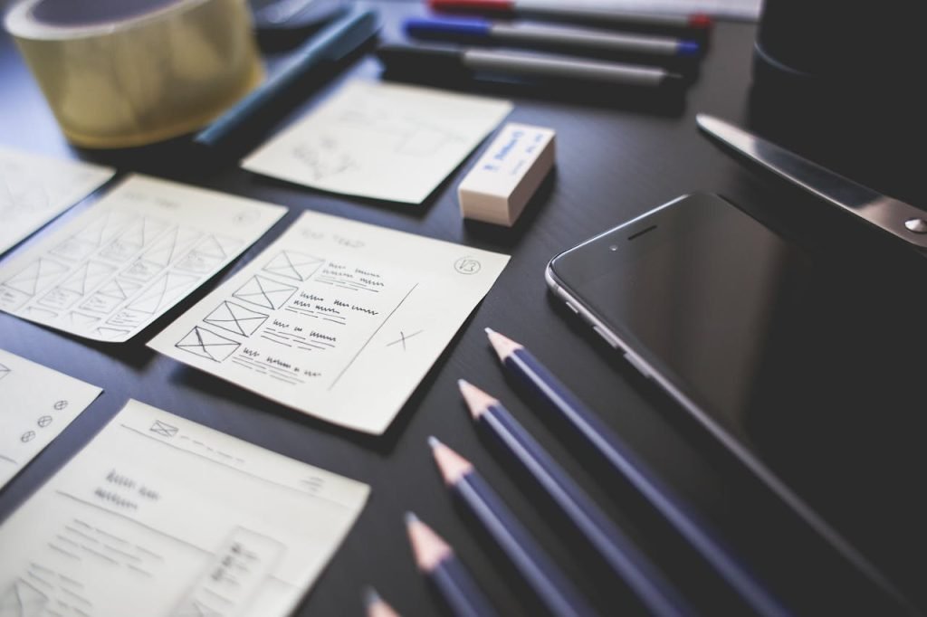 A creative workspace featuring UI design plans, pencils, a smartphone, and other office tools.